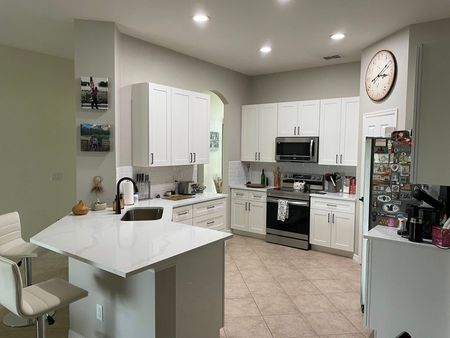 A kitchen with white cabinets , stainless steel appliances and a clock on the wall.