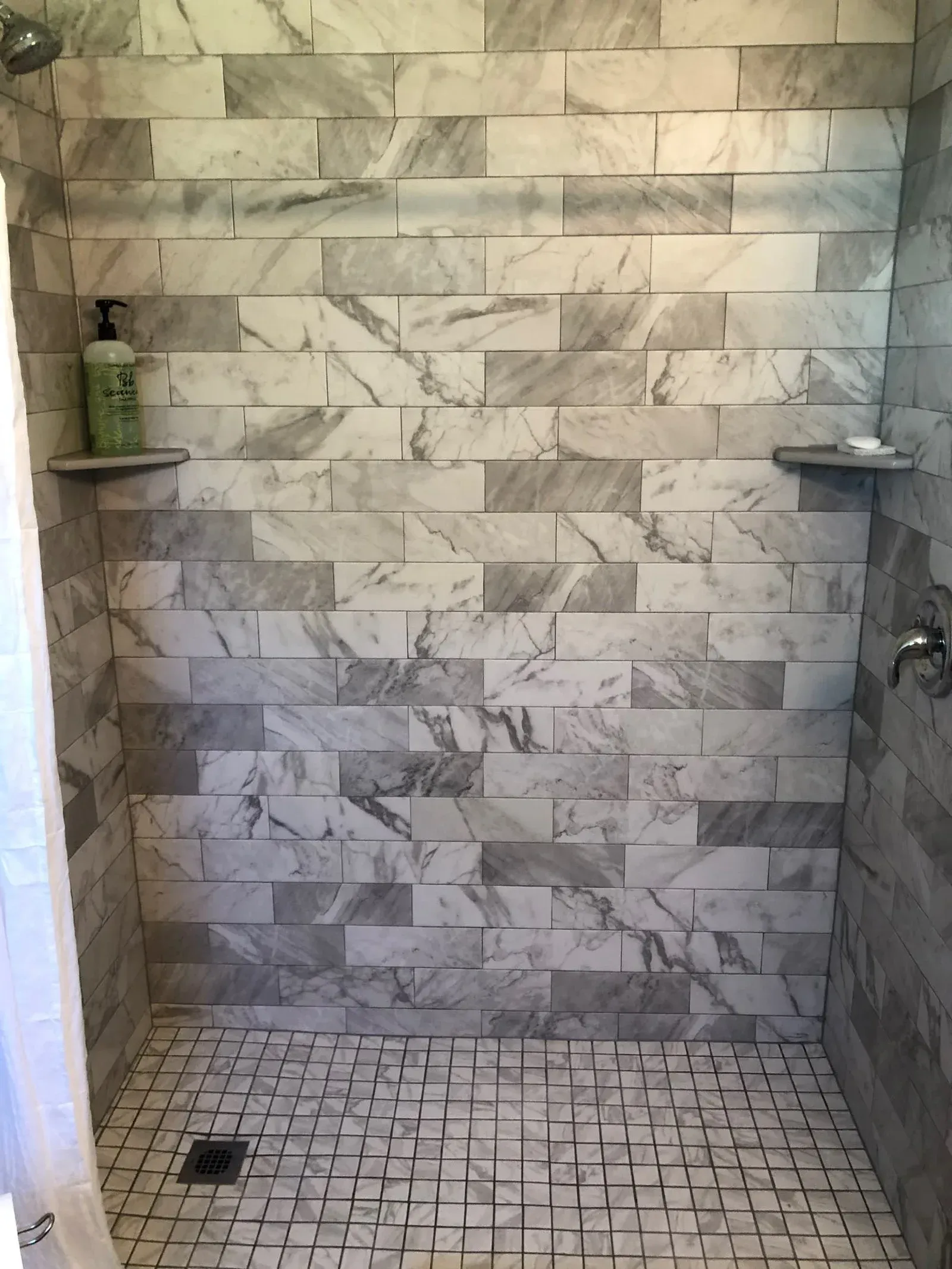 A shower with a tiled floor and a marble wall.