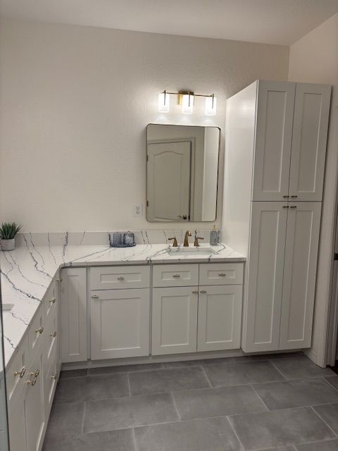 White bathroom with vanity, countertop, mirror, cabinet and grey tile floor.