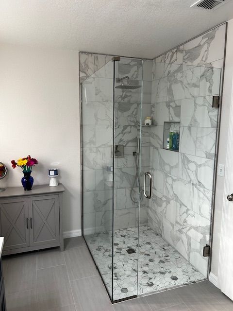 A modern bathroom with a marble-tiled shower, glass doors, and a gray vanity with flowers.