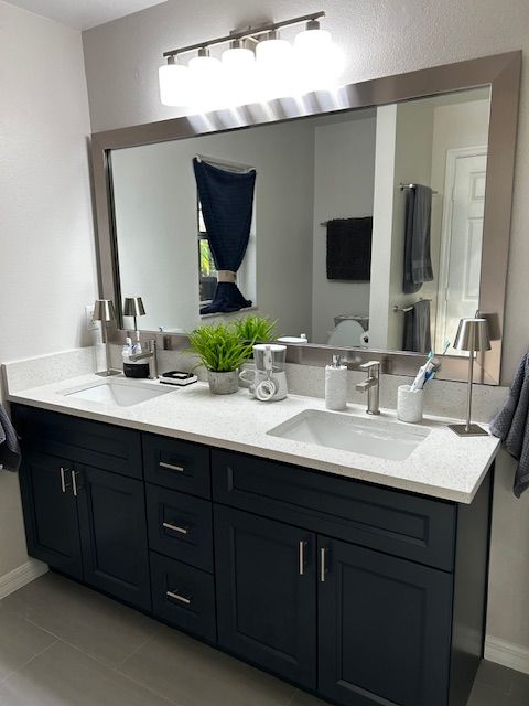 Dark blue bathroom vanity with a white countertop, large mirror, and brushed nickel hardware.