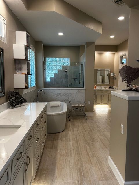 Spacious, modern bathroom with white countertops, beige cabinets, and a freestanding tub.