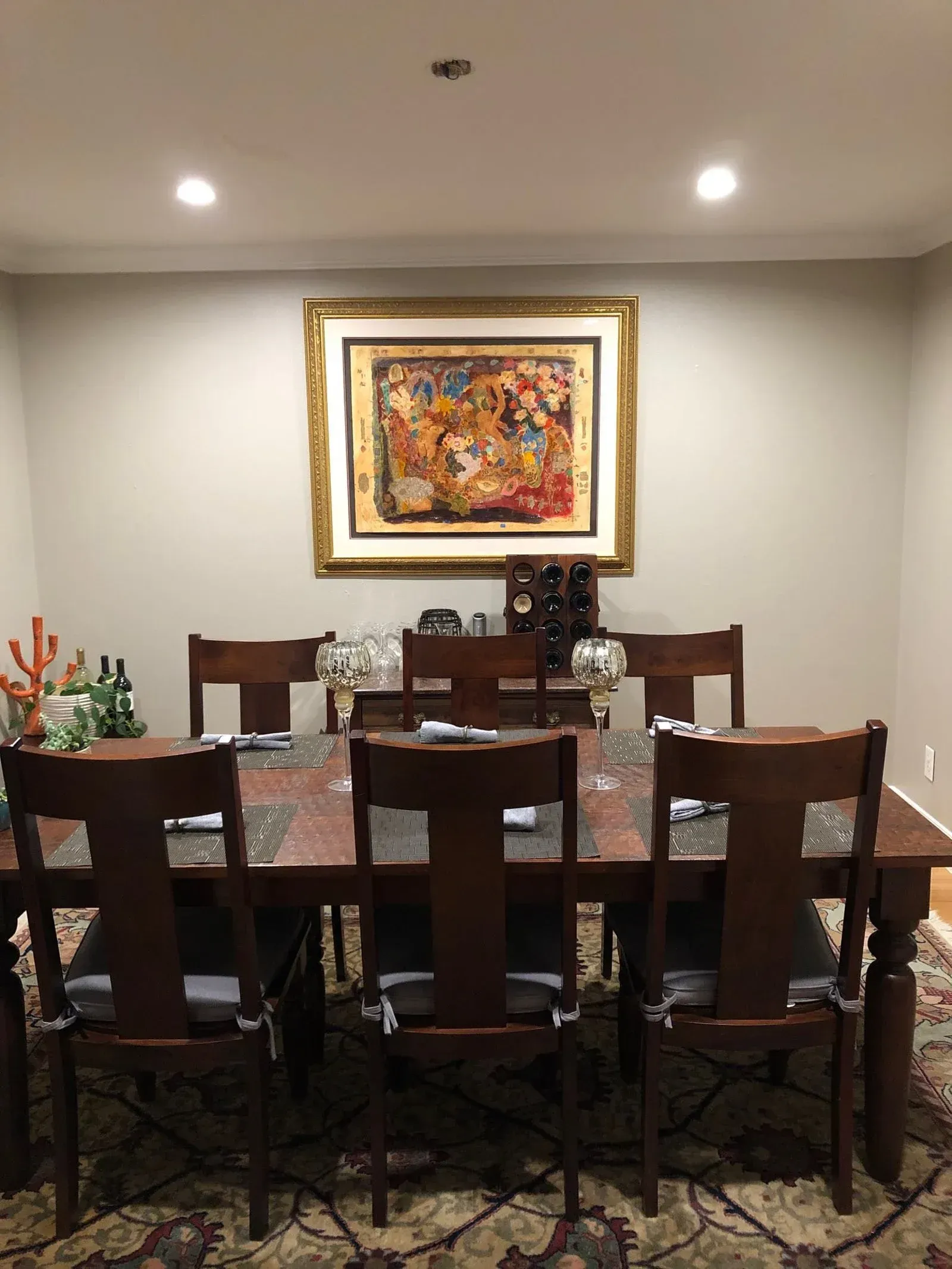 A dining room with a table and chairs and a painting on the wall.