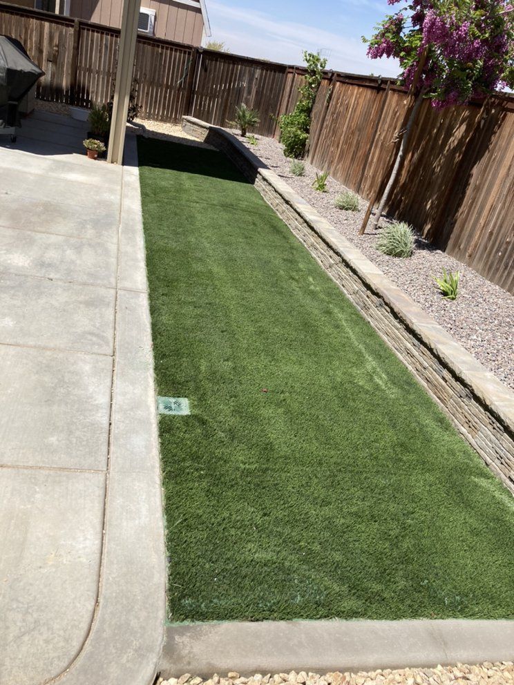 Artificial grass lawn with concrete border. Wooden fence backdrop and small plants.