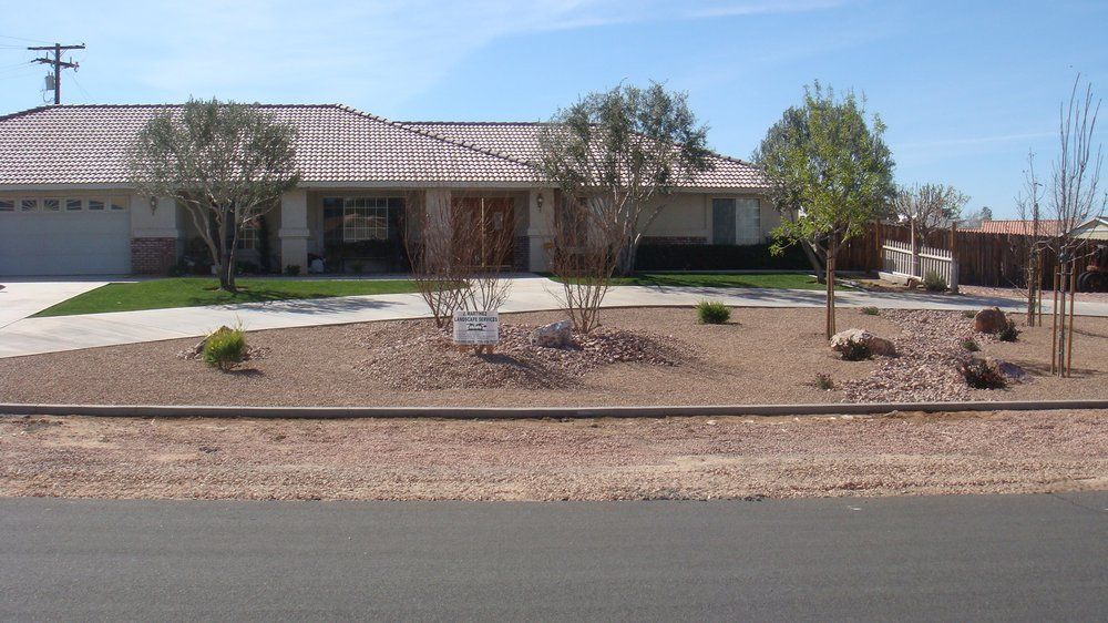 Ranch-style house with tan siding, brown tile roof, and front yard with gravel landscaping and several small trees.