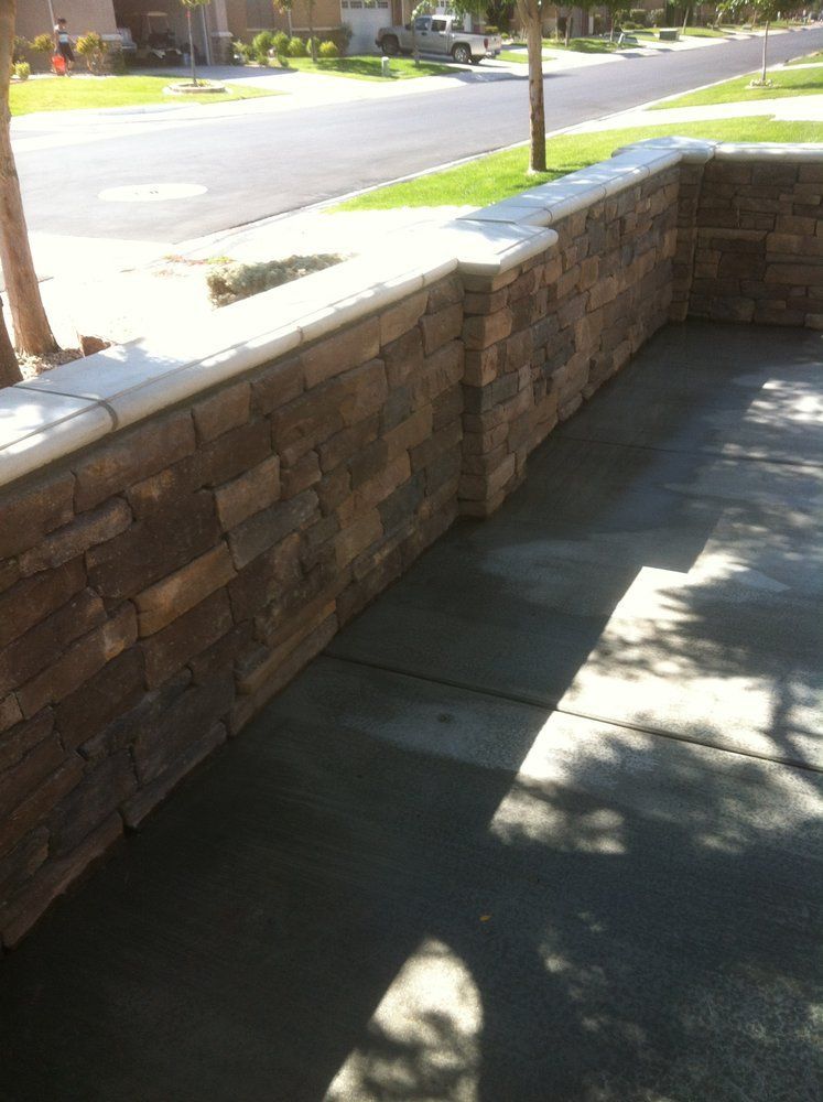 Stone wall along a driveway, topped with a white border, sunny day.