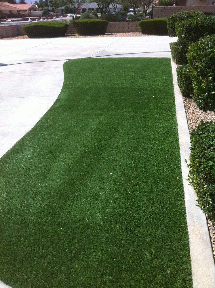 Green artificial turf alongside a concrete driveway and neatly trimmed bushes.