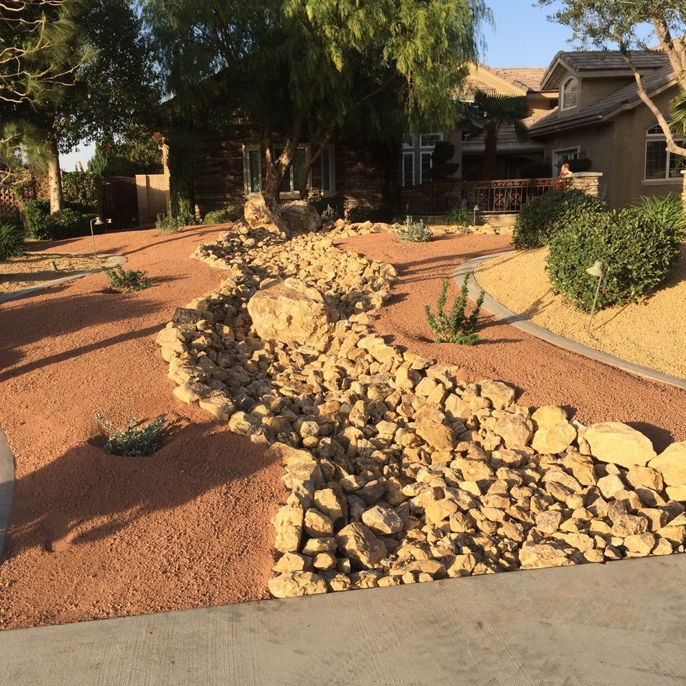 Driveway with dry creek bed, tan gravel, large rocks, and house in background.