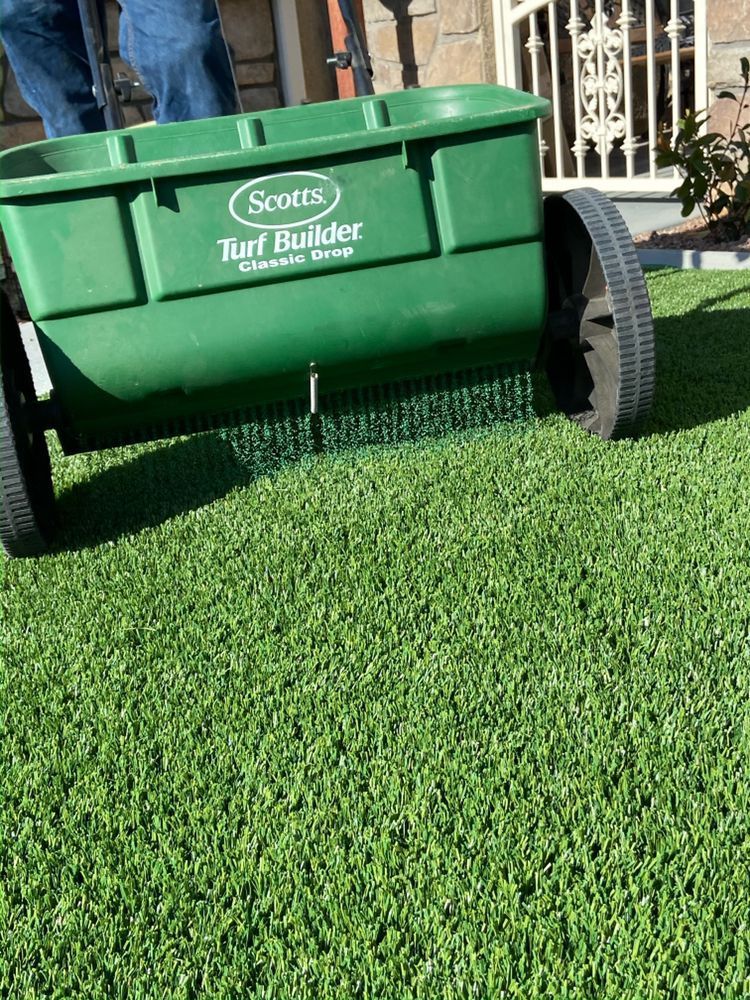 Green fertilizer spreader on lawn, applying granules.