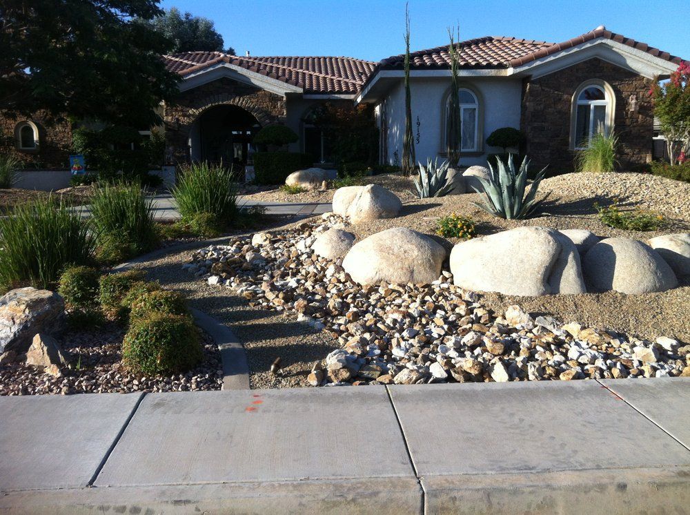 House with rock landscaping and drought-tolerant plants along the sidewalk.