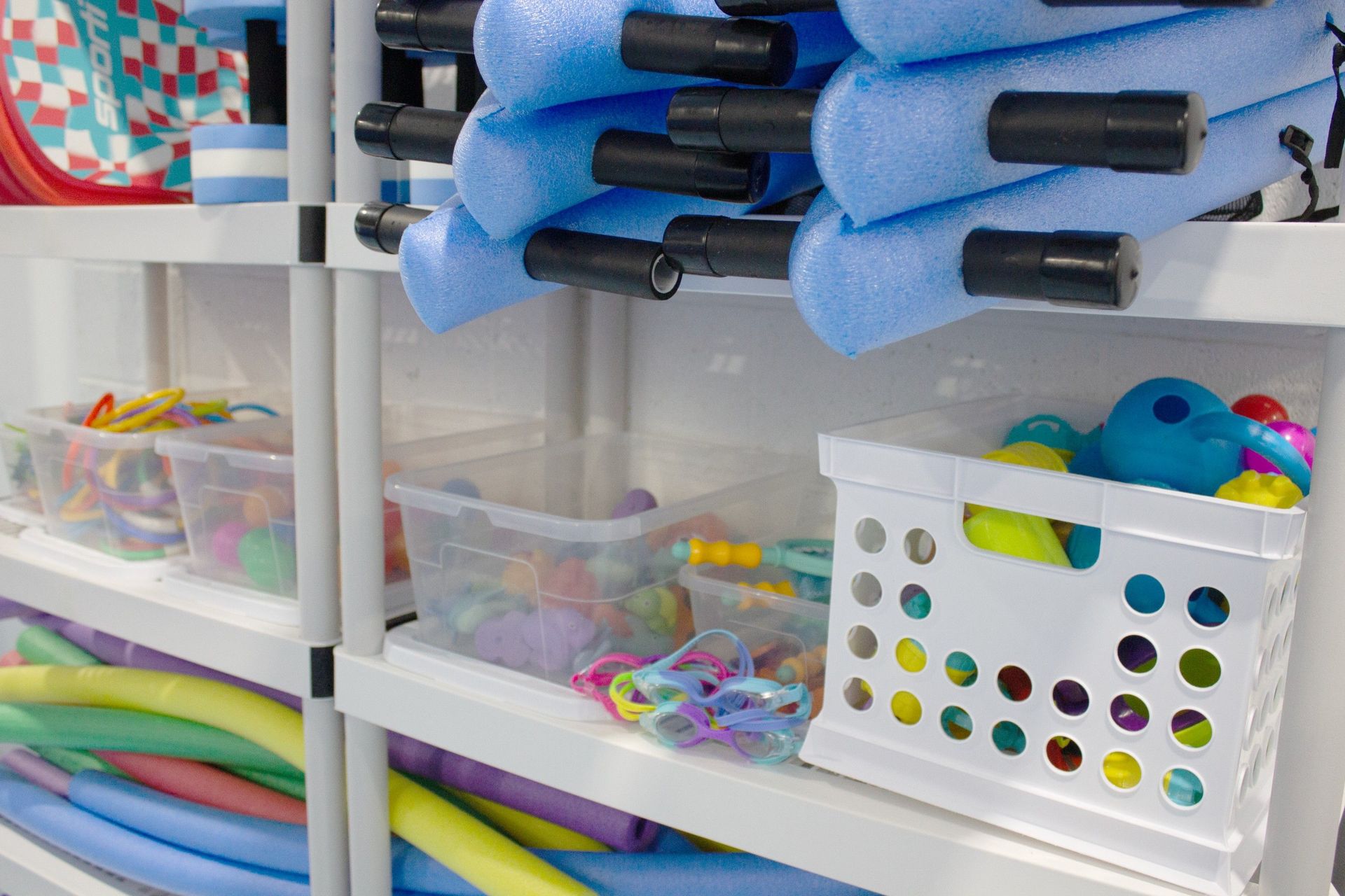 A shelf filled with lots of toys , including foam noodles.