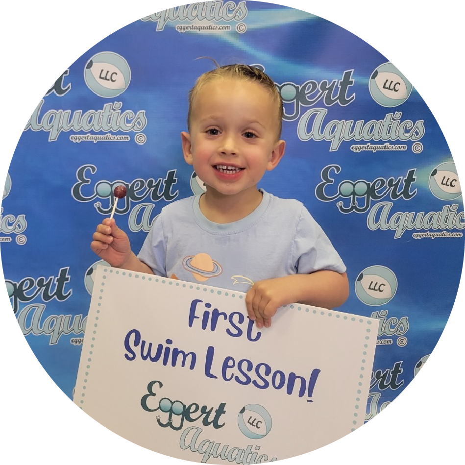 A young boy is holding a sign that says first swim lesson
