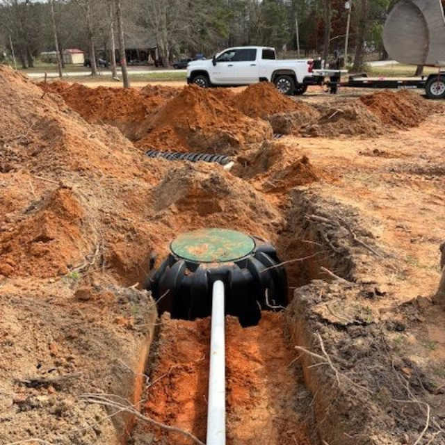 Man in blue overalls pumping a septic tank with a large hose, grassy outdoors setting.