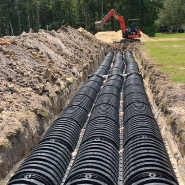 Green septic tank lid in a dirt hole, surrounded by grass.