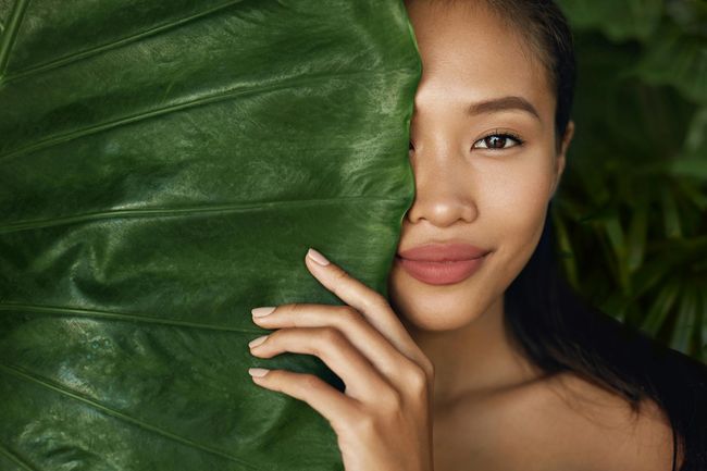 Woman with natural makeup behind green leaf
