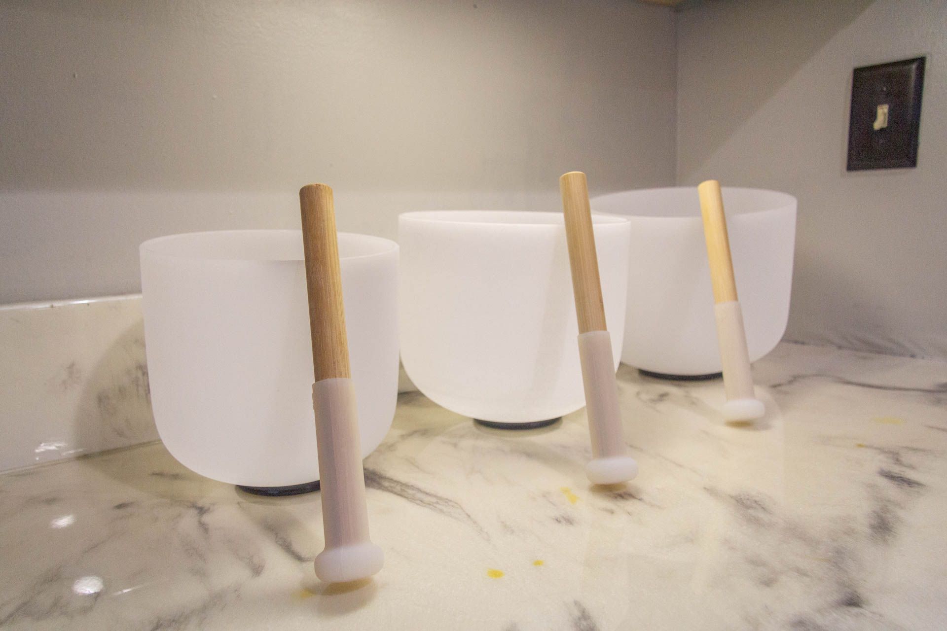 three crystal singing bowls with wooden handles are sitting on a marble counter .