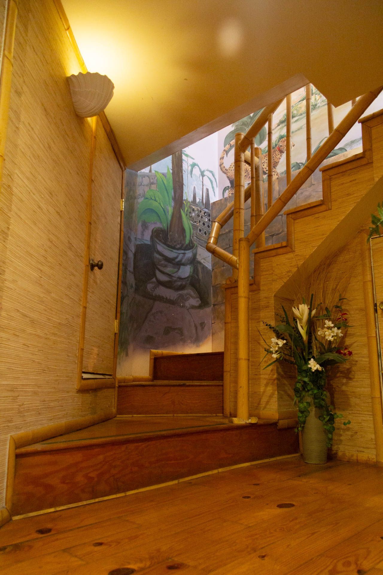 a wooden staircase with a painting on the wall and a vase of flowers on the floor .
