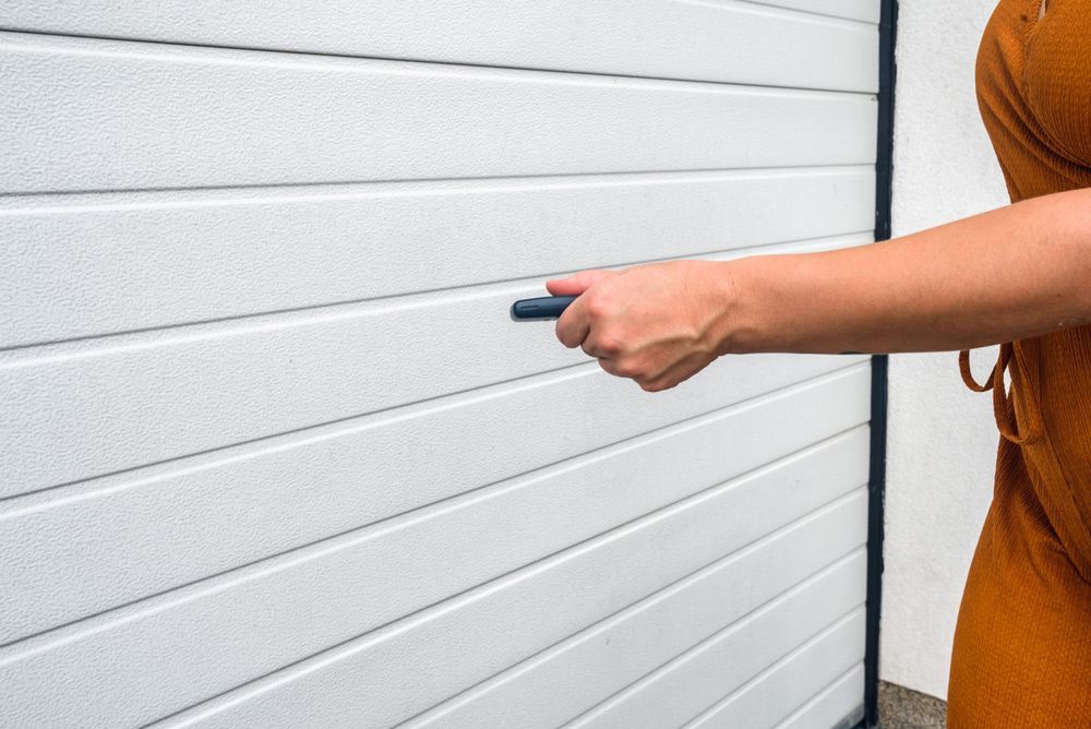 A Woman Is Opening A Garage Door With A Remote Control — Lighthouse Beach Garage Door Service in Bonny Hills, NSW