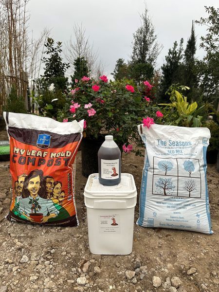 A bag of compost , a bucket , and a bottle are sitting on the ground.