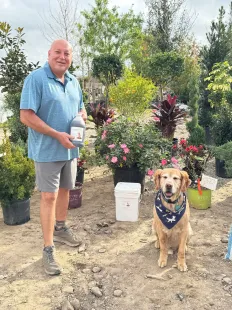 A man is standing next to a dog in a garden.