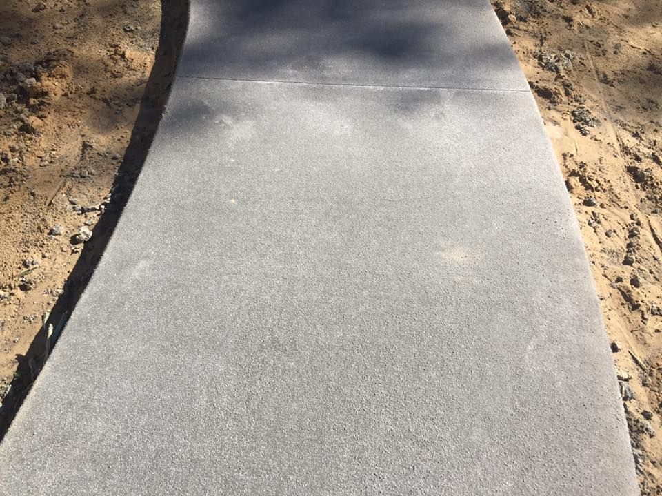 Concrete sidewalk with rough texture, bordered by dirt and shadows.