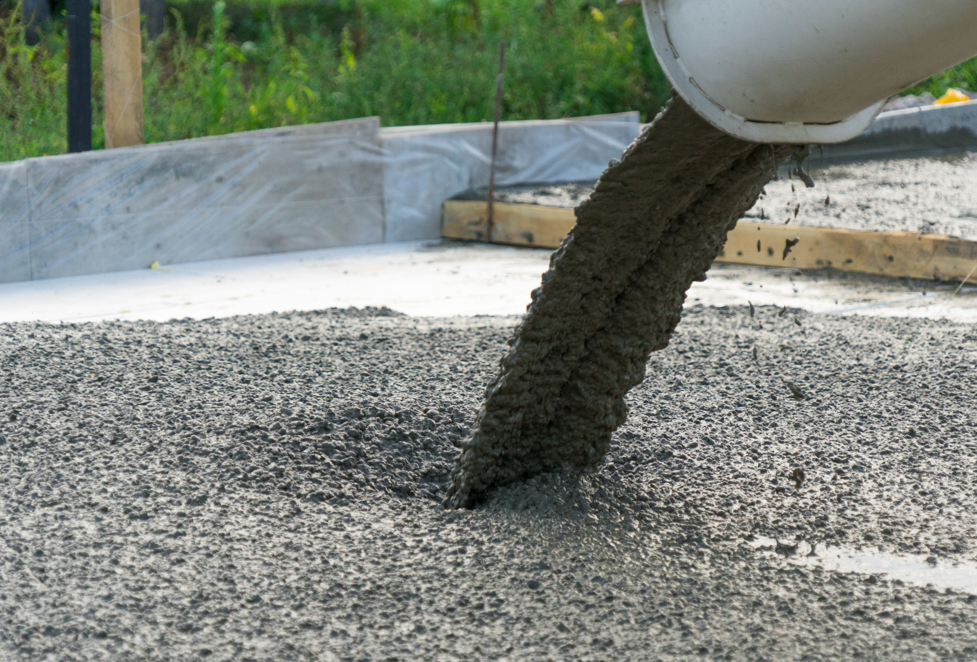 Concrete pouring from a white chute onto gravel in an outdoor setting.