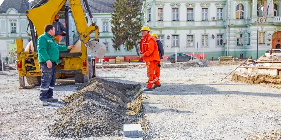 Two construction workers are standing next to a yellow excavator on a construction site.