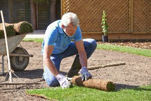 A man is kneeling down to roll out a roll of turf.