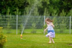 A little girl is playing with a sprinkler in her backyard.