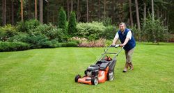 A man is pushing a lawn mower on a lush green lawn.
