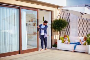 A man is opening a sliding glass door to a patio with a woman sitting on a couch.