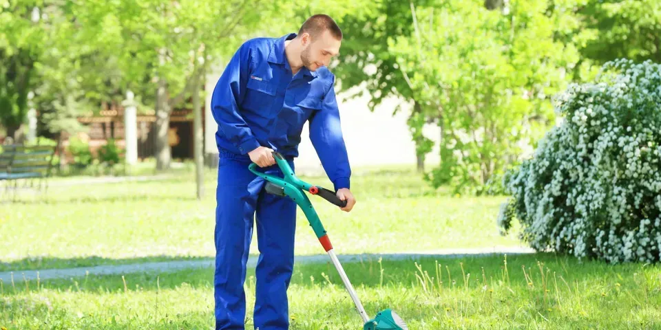 A man is cutting grass with a lawn mower in a park.