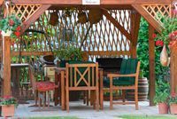 A wooden gazebo with a table and chairs underneath it.