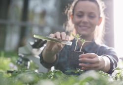A woman is holding a potted plant and a test tube.