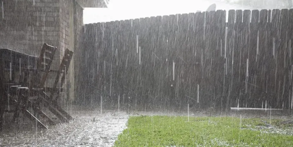 A backyard with a fence and chairs in the rain.