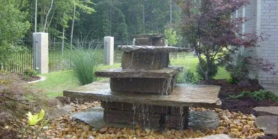 A water fountain is sitting on top of a pile of rocks in a garden.