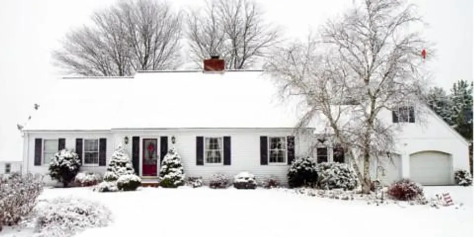 A white house with a red door is covered in snow.