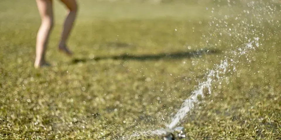 A woman is running through a sprinkler in a field.