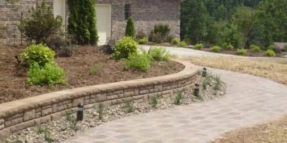 A brick walkway leading to a house with a stone wall.