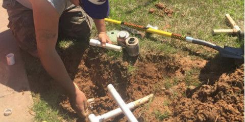 A man is kneeling down in the dirt with a shovel.