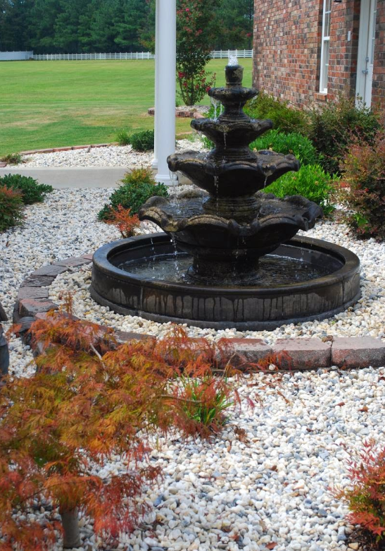A fountain in a gravel area in front of a house