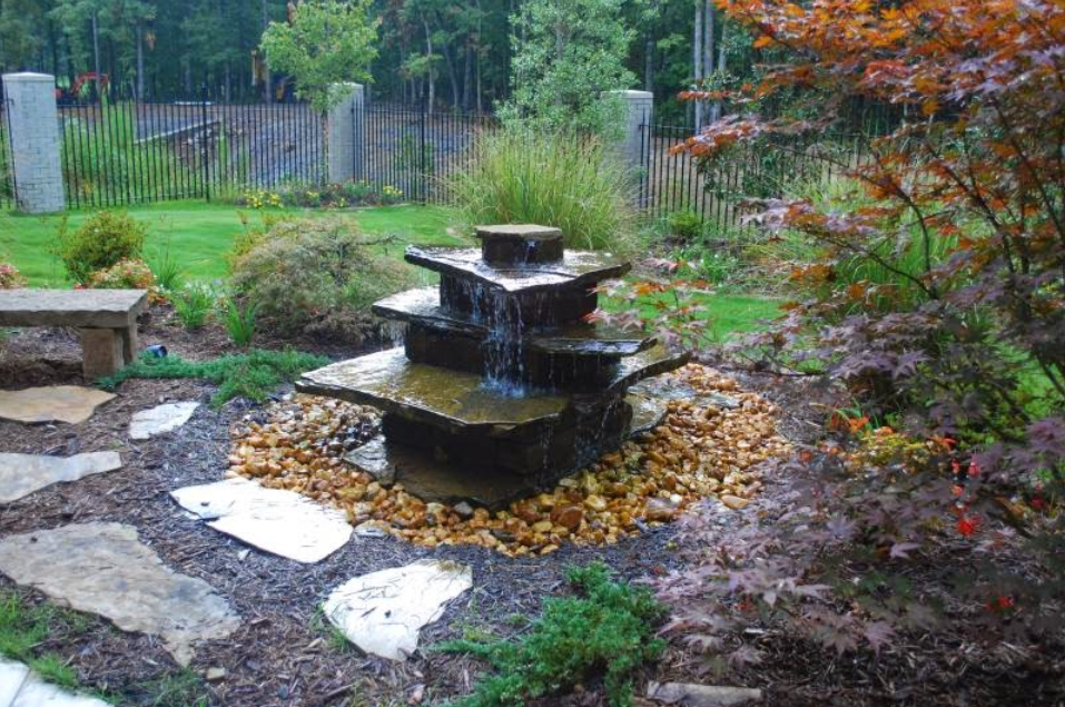 A water fountain in a garden with a bench in the background.