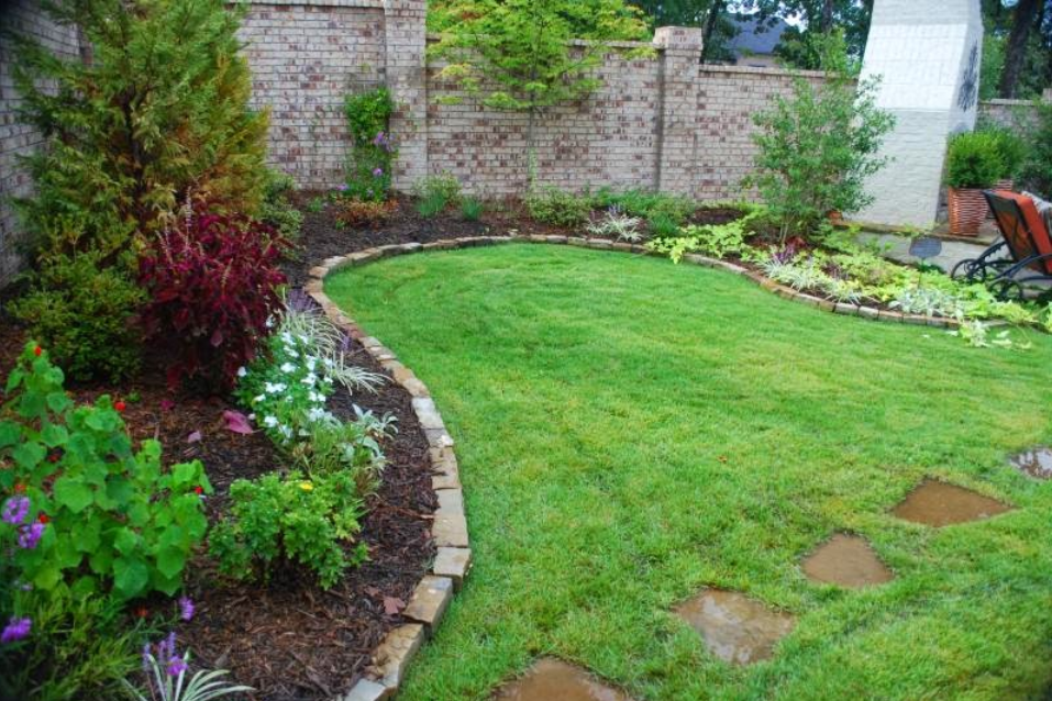 A backyard with a lush green lawn and a brick wall.
