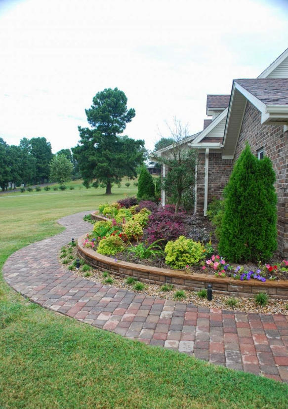 A brick walkway leading to a house with a garden in front of it.