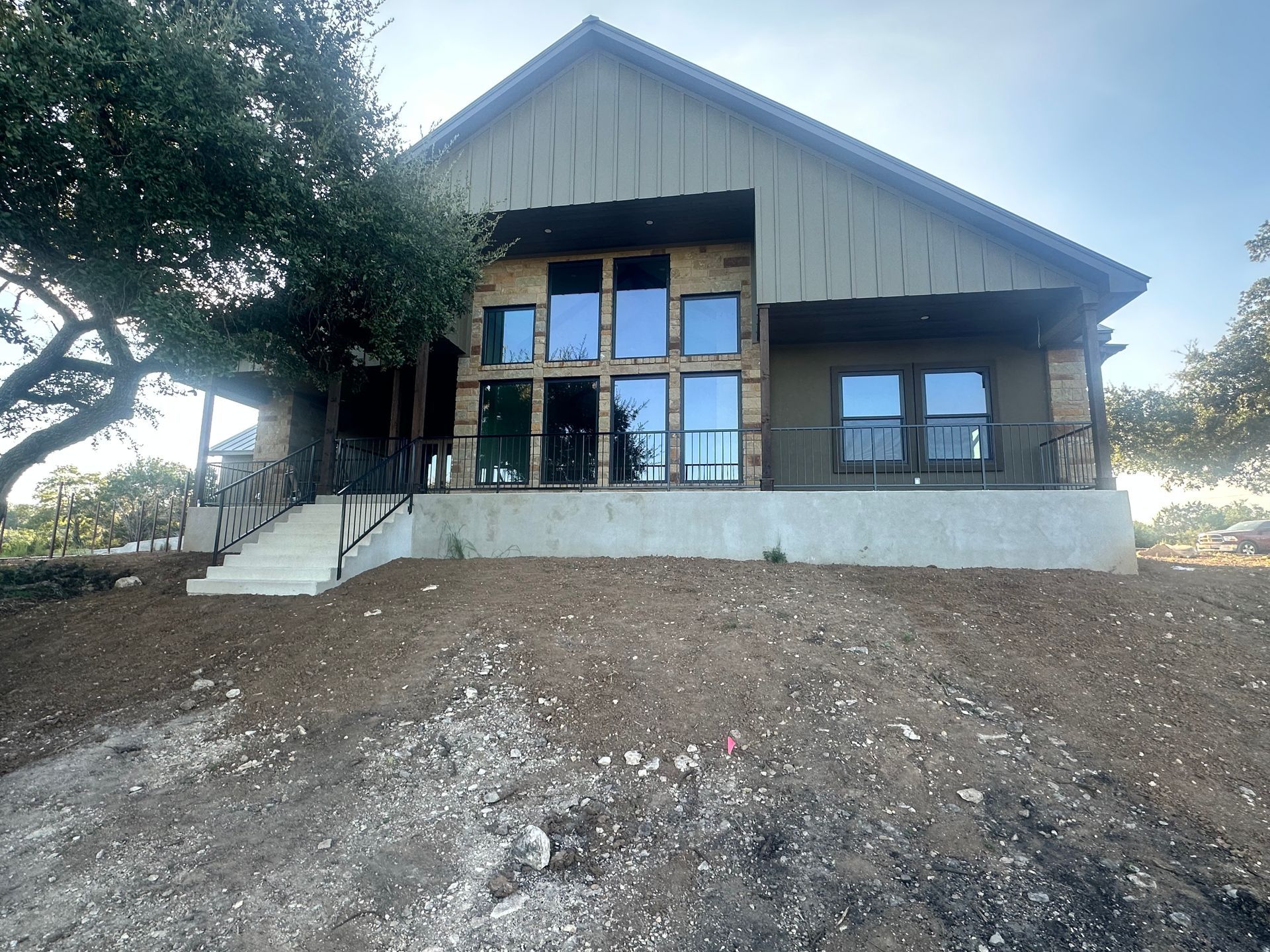 Modern house with large glass entry, sloped roof, and concrete steps on a dirt hillside.