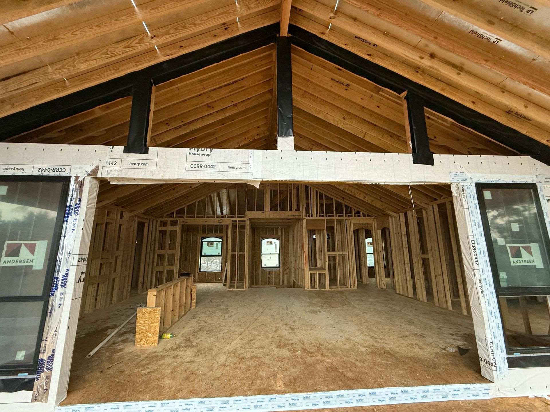 Unfinished house interior with exposed wood framing and open front entrance under a gabled roof.