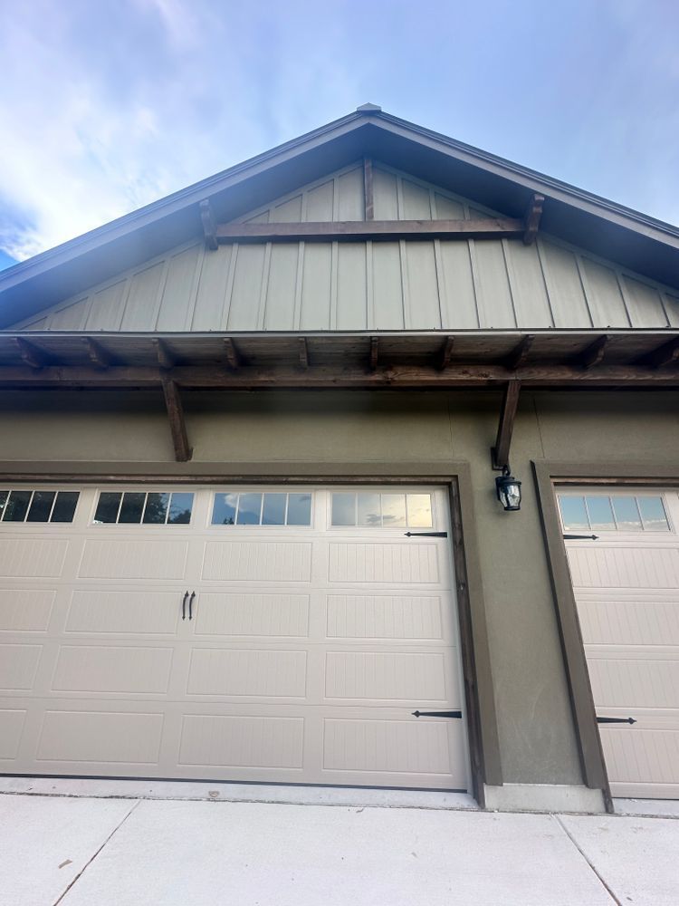 Snow-covered garage with beige siding and white double doors under a peaked roof