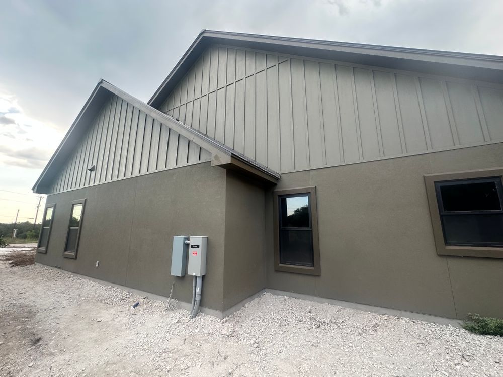 Exterior of a new gray building with white gabled siding and gravel around the foundation
