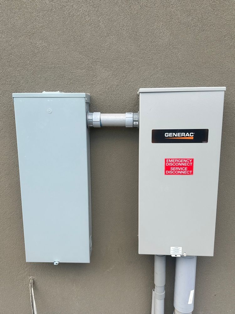 Two gray utility electrical boxes mounted on a beige exterior wall, connected by white conduit.