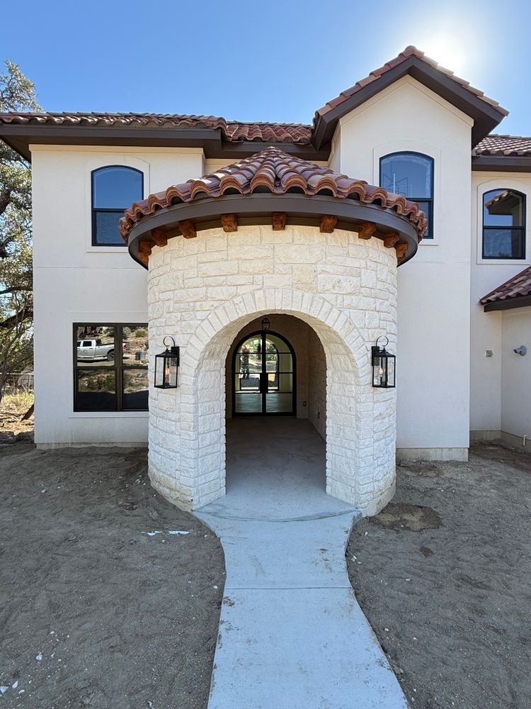 Front entrance of a house with a white stone archway and red tile roof above a curved walkway